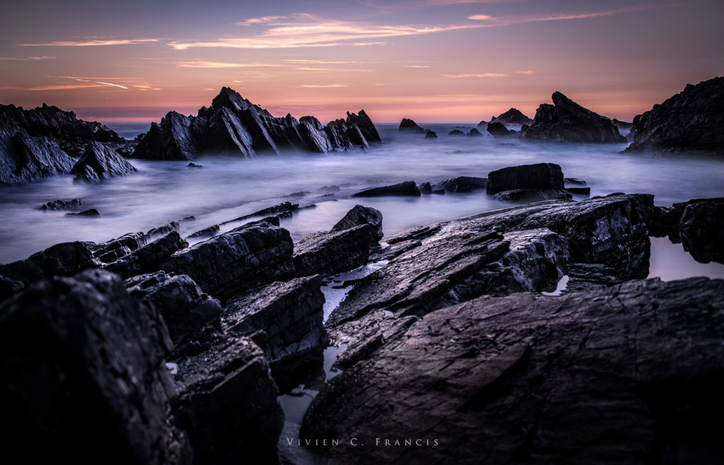 Dark rock formations with a orange red sunset by the sea