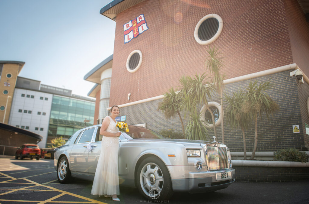 Bride holding yellow flowers standing in front of silver car with palm trees in background