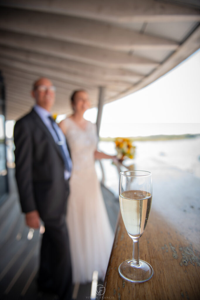 Champagne glass with a wedding couple in background watching the view over the sea