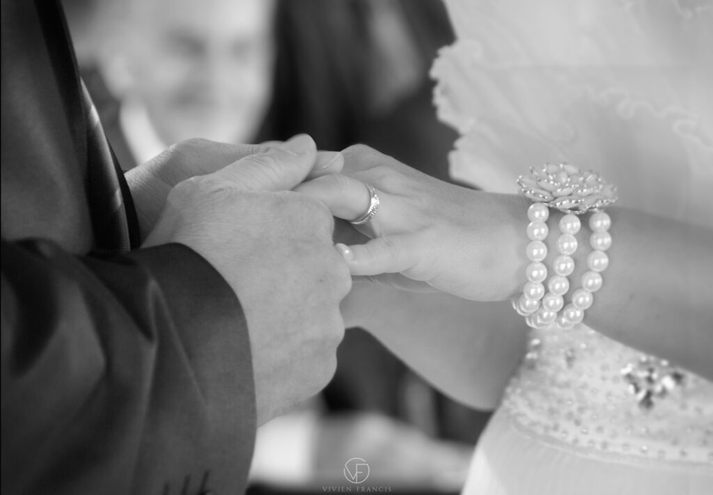 Man holding a woman's hand with a ring around her finger wearing white pearls and white dress
