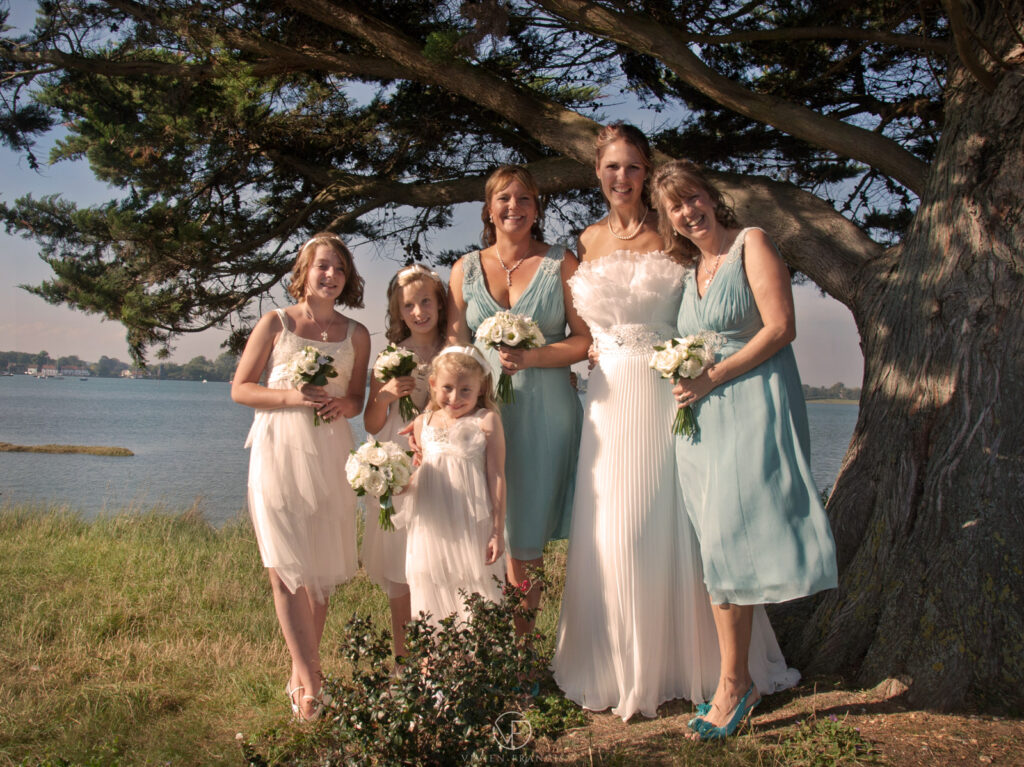 Bridesmaids wearing blue and white dresses standing together outside by a tree