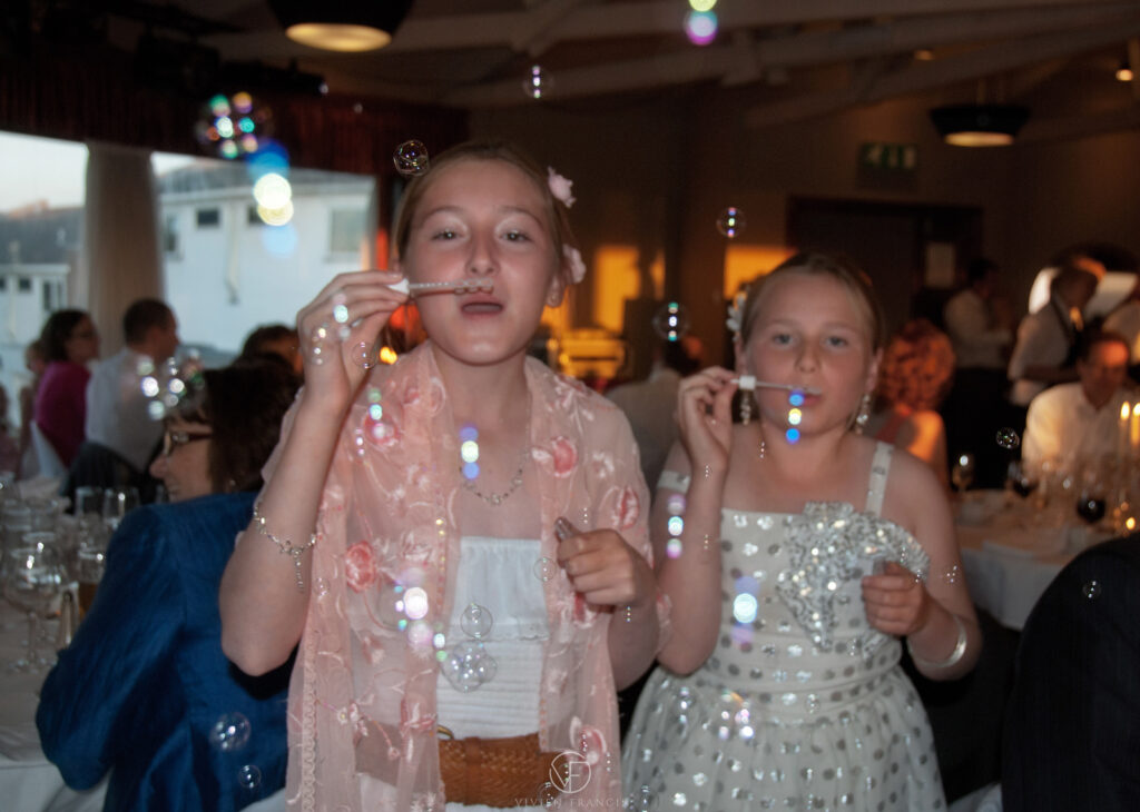 Two girls blowing bubbles wearing pretty dresses with people having dinner