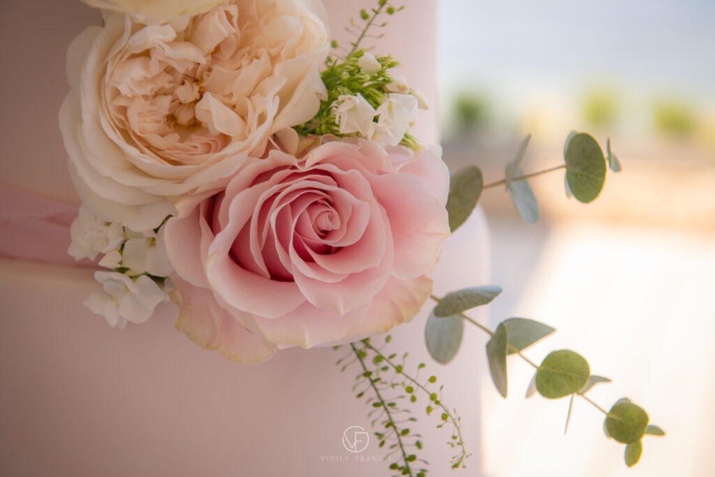 Pink and white roses on a wedding cake with a pink ribbon