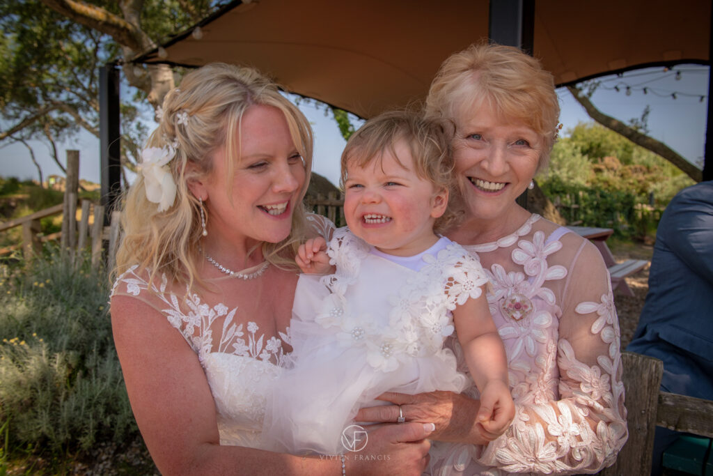 Mother of the bride, bride and daughter all dressed in white smiling together