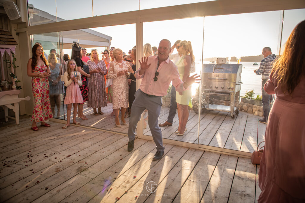 Groom in pink shirt and silver trousers making a funny gesture with his hands and dancing