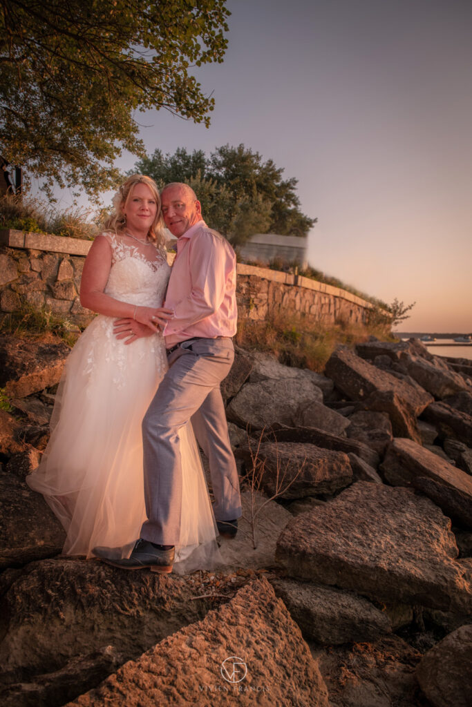 Bride and groom standing on rocks by the beach holding each other