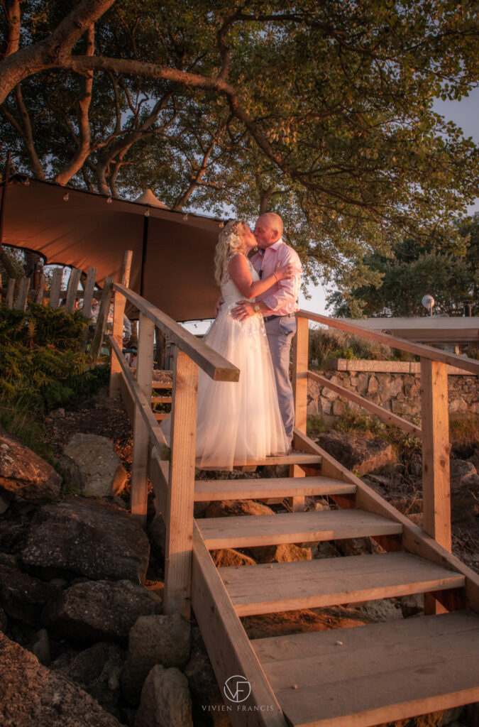 Bride and groom outside venue standing on wooden stairs with tent and trees in the background