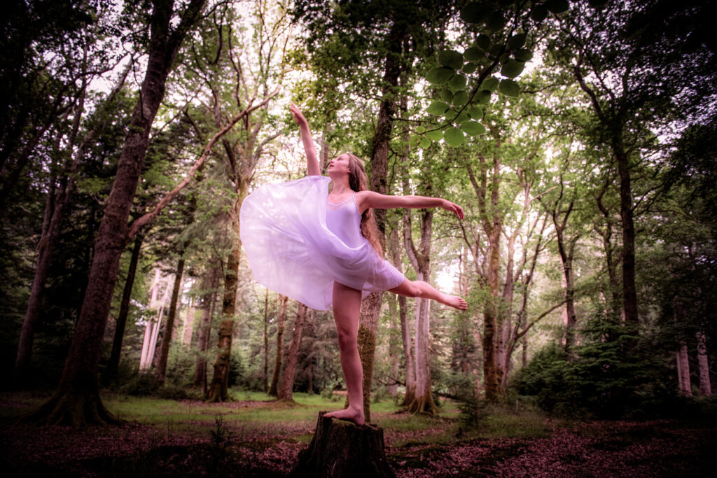 Young lady standing on a tree stump flinging her white dress into the air and striking a pose