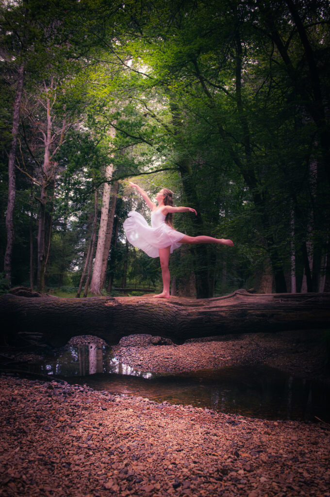 Girl standing on a tree over a little flow of water in a forest, with a bit of sunlight through the leaves of the trees
