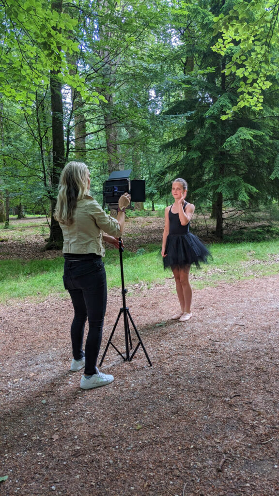 Woman adjusting a light directed at a girl standing in a black dress between tall trees