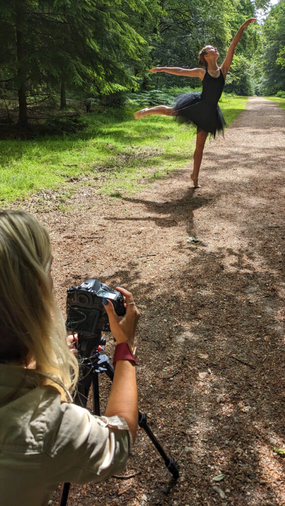 Woman with blonde hair using a camera taking a photo of a girl doing a ballet pose